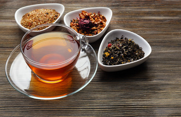 Tea concept. Different kinds of dry tea in ceramic bowls. Glass cup of tea on wooden background