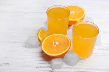 Two orange juices with cubes of ice and orange on white wooden table background, closeup