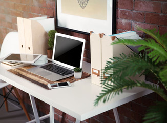 Workplace with table and different devices on brick wall background