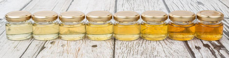 Different grade and color of honey in mason jar over wooden background