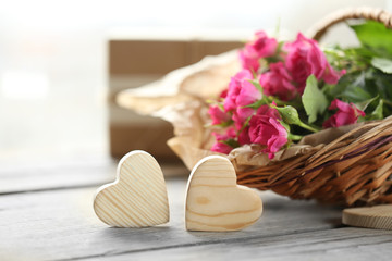 Pink roses in a wicker basket and wooden hearts on a white table, close up