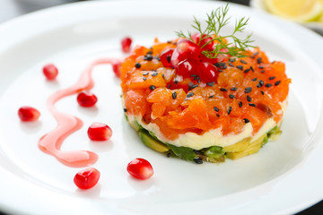 Fresh tartar with salmon and avocado and pomegranate seeds on white plate, close up