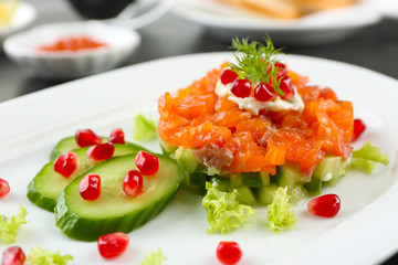 Fresh tartar with salmon, cucumber and pomegranate seeds on white plate, close up