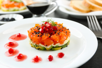 Fresh tartar with salmon, avocado and  pomegranate seeds on white plate, close up