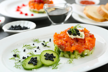 Fresh tartar with salmon, cucumber and black caviar on white plate, close up