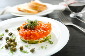Fresh tartar with salmon, avocado and capers on white plate, close up