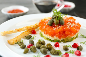 Fresh tartar with salmon, avocado and capers on white plate, close up