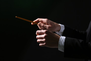 Music conductor directing with baton on black background, close up