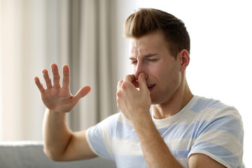 Young blonde man pinching his nose because of the stench in the room