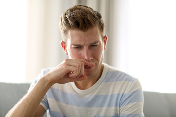 Fototapeta na wymiar Young blonde man pinching his nose because of the stench in the room
