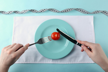 Female hands holding knife and fork on plate with single cherry tomato, top view