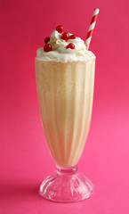 Glass of milk cocktail with cream and berries on pink background
