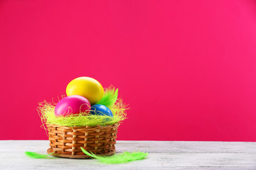 Colorful Easter eggs in wicker nest on pink background