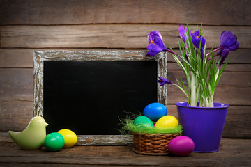 Easter eggs with crocus flowers and blackboard on wooden background