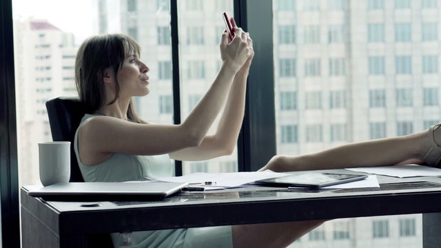 Businesswoman taking selfie photo with smartphone by desk in the office
