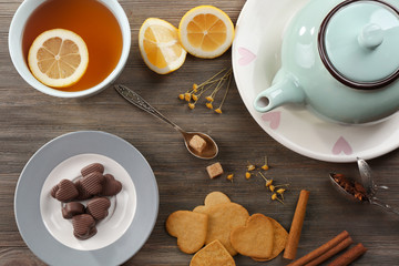 Cup of brewed tea with lemon and sweets on wooden table
