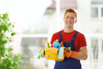 Young janitor holding cleaning products and tools on tub in office