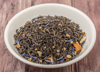 Dried black Earl Grey tea leaves in white bowl over wooden background