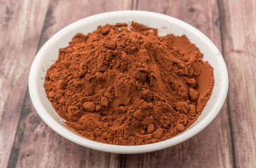 Cocoa powder in white bowl over wooden background