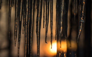 Abstract background of natural icicle formation through glass as morning sun rises.  Long icicles on a wintry January morning. Sunshine dawning through icicles that hang low from a roof's edge.