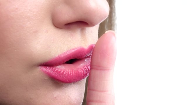 Finger on lips - silent gesture. Woman holding her finger to her lips in a gesture for silence. Closeup