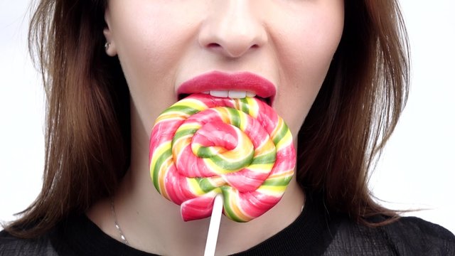 Woman licks candy with beautiful make-up isolated on white background. Closeup