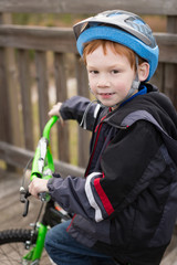 Fototapeta na wymiar Happy little boy wearing a helmet riding a bicycle across a wooden bridge.