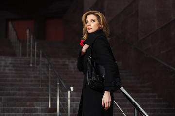 Fashion blond woman in black coat on the steps