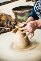 Closeup view of hands of a senior asian potter forming clay into a pot on a turntable. Image of asian handcrafts and manuafacture.