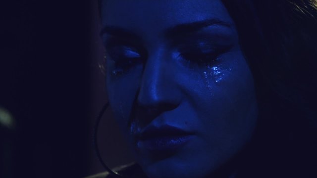 Desperate sad girl cyring in disco club with cold lights. Close up.