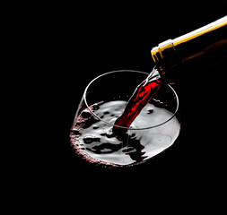 Pouring red wine into the glass against black background
