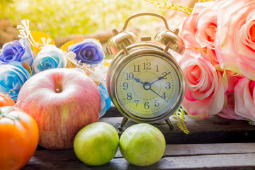 The vintage clock with pink rose and fruits in background
