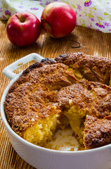 Apple pie in a white baking dish on the wooden background.