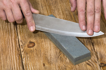 Hands holding knife and whetstone on  the wooden board