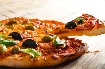 Rustic pizza with salami, olives and fresh herbs lifted slice