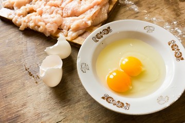 Broken eggs in a plate and chicken meat 