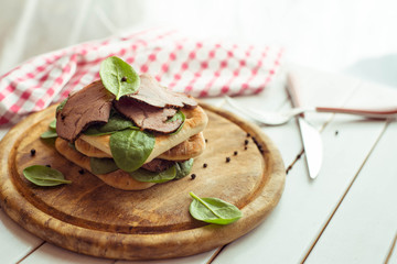 Roast beef sandwich with salad and pepper on rustic wooden plate. The toning.