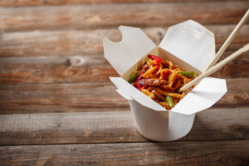 Noodles with pork and vegetables in take-out box on wooden table