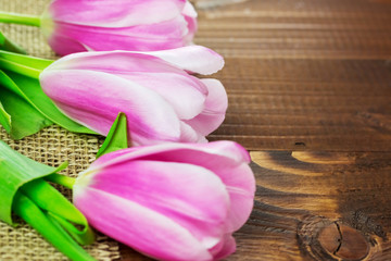 beautiful pink tulips lying on the burlap on the background of old brown boards. The idea of Mother's day cards, March 8, birthday with free space for your text