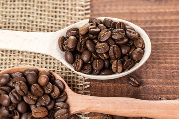 whole coffee beans in a wooden spoon and a scattering of coffee beans on burlap and old brown boards