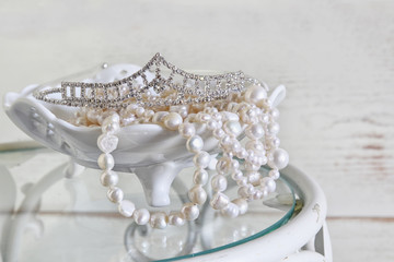 high key image of white pearls necklace and diamond tiara on vintage table
