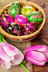Fototapeta na wymiar Beautiful background with painted Easter eggs in a wicker basket and lined with tulips on the background of burlap and old brown boards with free space for your text