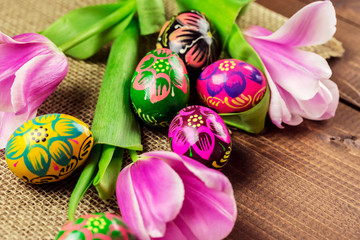 Beautiful background with painted Easter eggs and tulips laid on a background of burlap and old brown boards with free space for your text