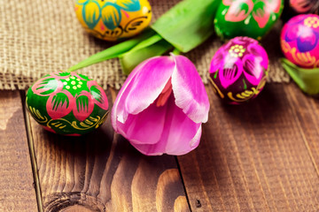 Beautiful background with painted Easter eggs and tulips laid on a background of burlap and old brown boards with free space for your text