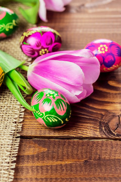 Beautiful background with painted Easter eggs and tulips laid on a background of burlap and old brown boards with free space for your text