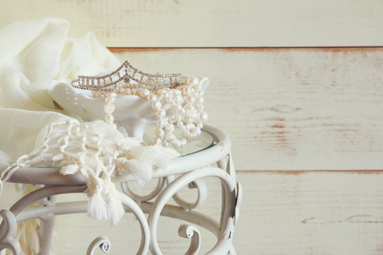 high key image of white pearls necklace and diamond tiara on vintage table
