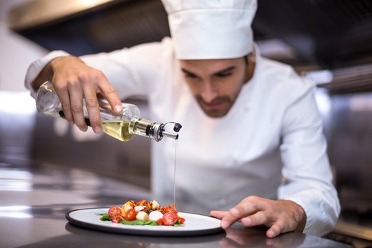 Handsome chef pouring olive oil on meal