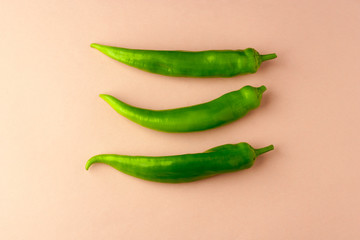 Three fresh green peppers on a pinkish natural paper background