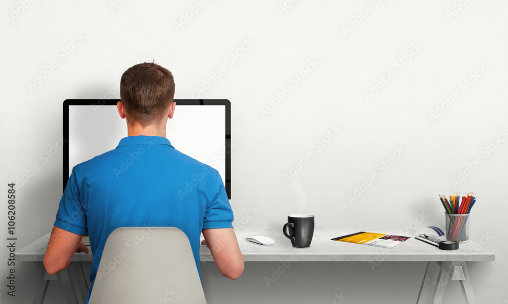 Poster Man working on computer with isolated screen in office interior. Work desk with keyboard, mouse, cup of coffee, paper, pencils. Free space on wall for text.