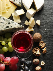 Different types of cheeses with wine glass and fruits.